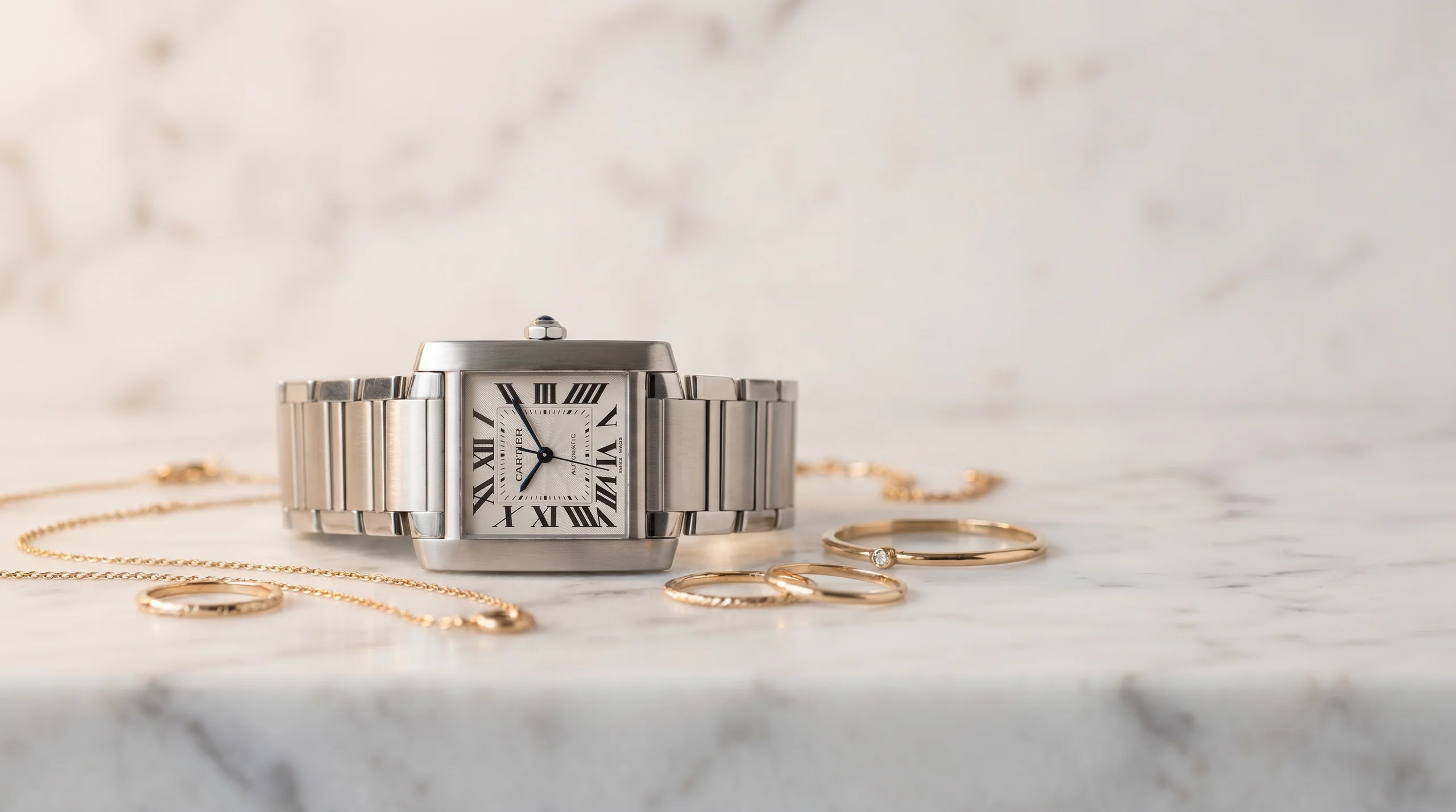 Cartier Tank Francaise in steel on a white marble surface beside fine gold jewelry