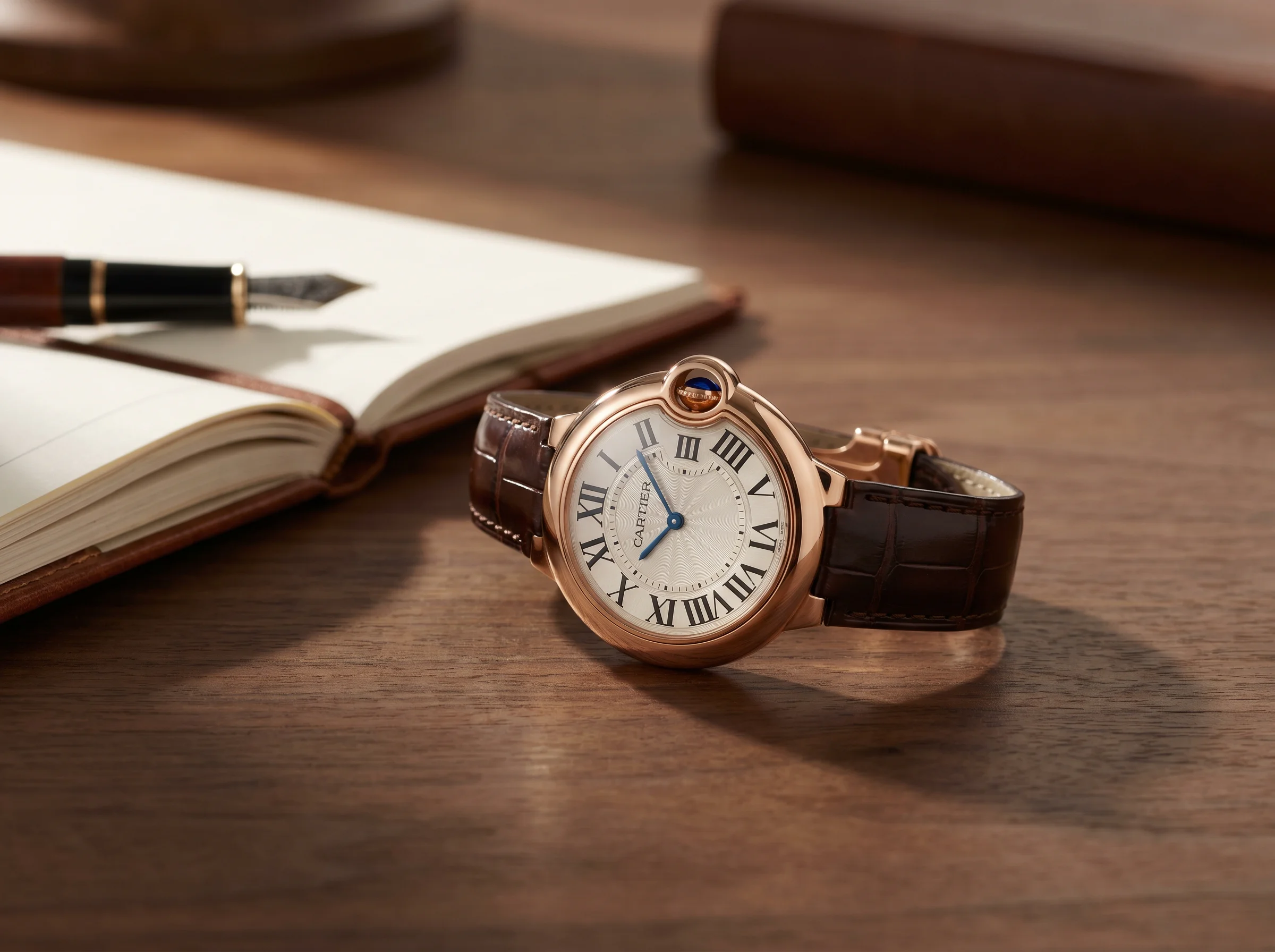 Cartier Ballon Bleu 40mm in rose gold on a brown alligator strap on a walnut desk
