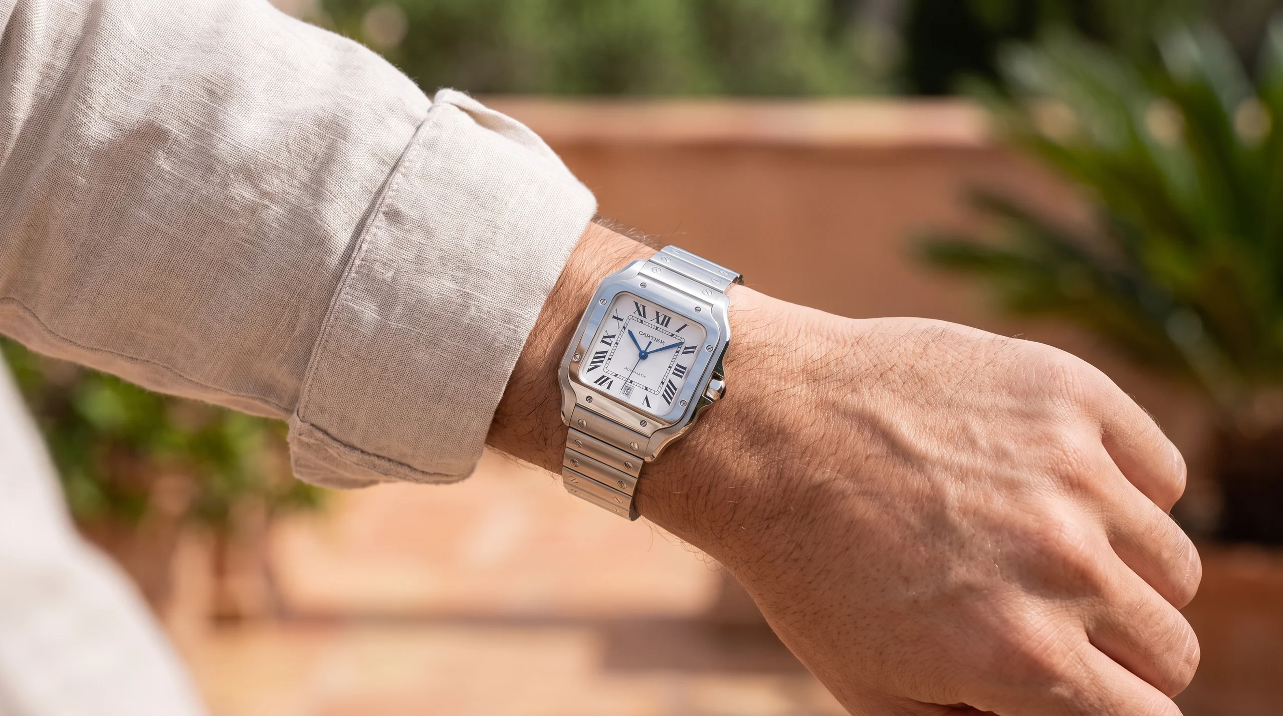 Steel Santos de Cartier worn on the wrist with a linen sleeve, showing its daily sport-luxury proportions
