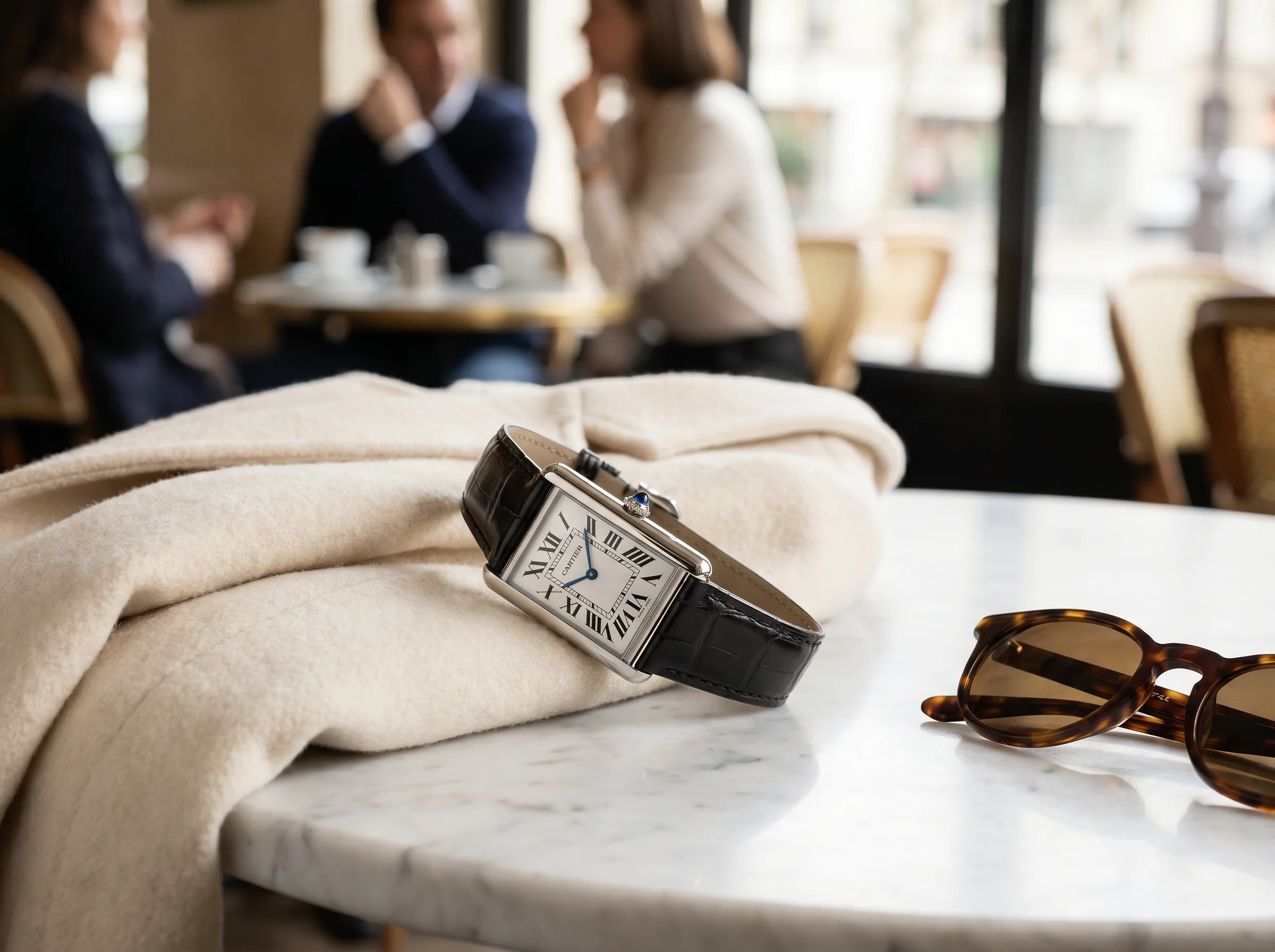 Cartier Tank Must WSTA0041 on a folded cream coat beside sunglasses on a marble cafe table