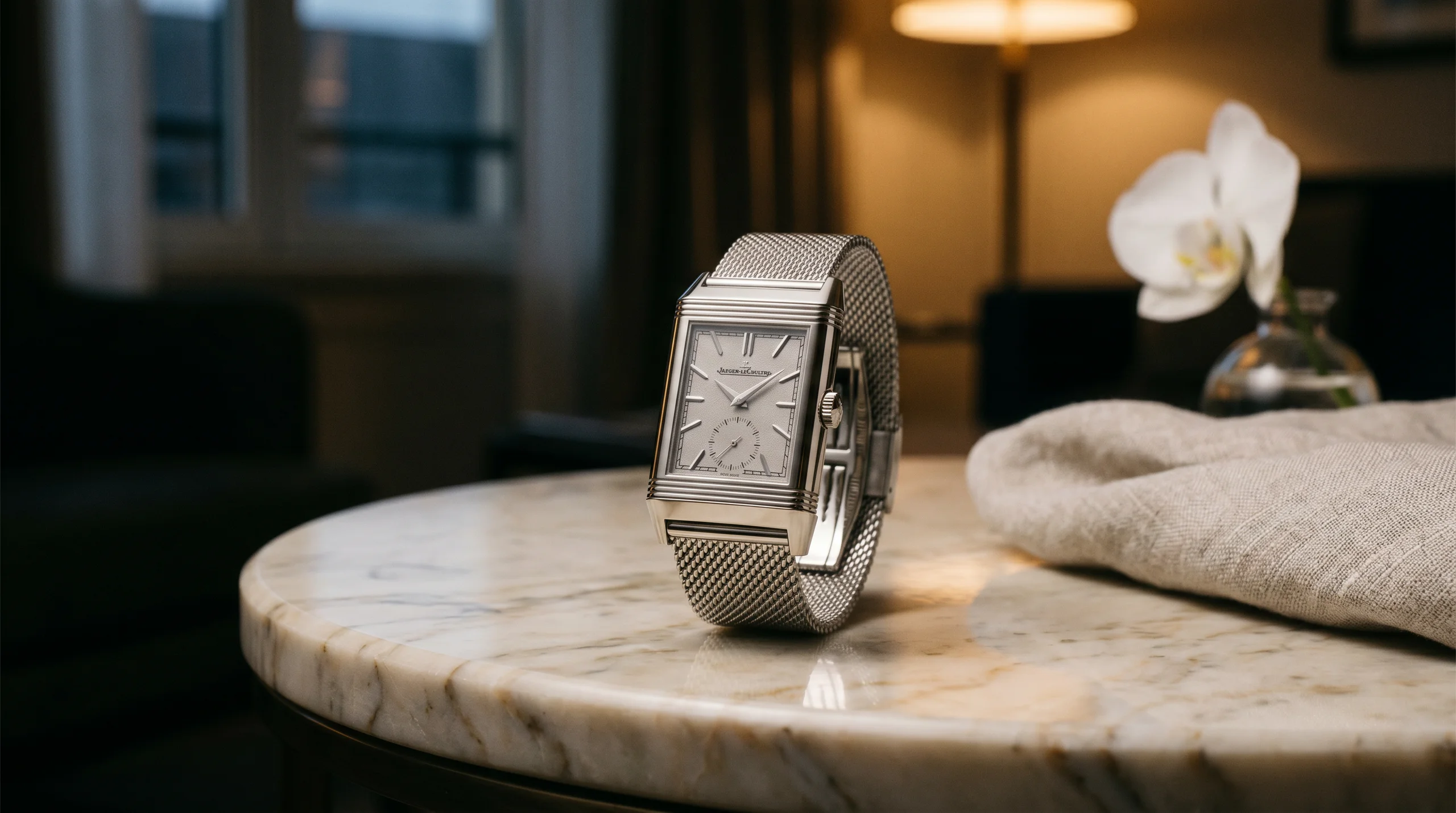 Jaeger-LeCoultre Reverso Tribute Monoface Small Seconds 'Or Deco' Q713312J in 18k white gold on Milanese mesh bracelet, resting on Carrara marble side table in evening light