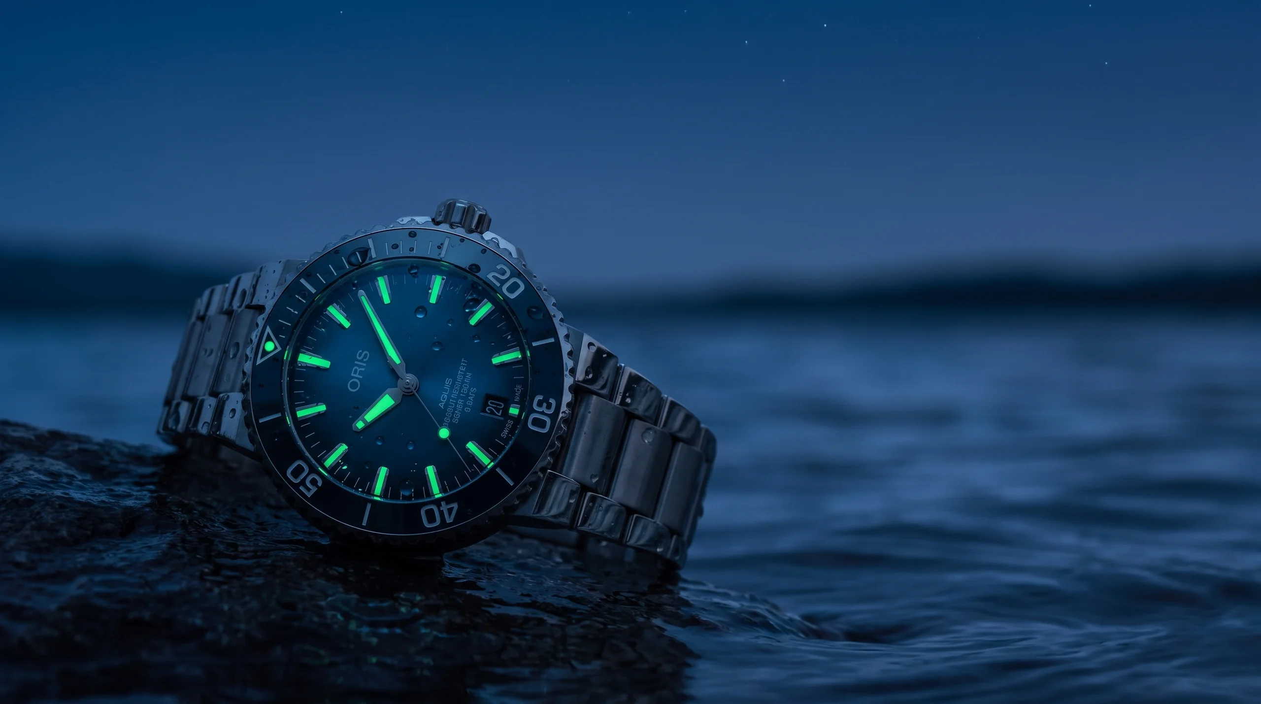 An Oris Aquis dive watch glowing green at dusk near water, lume doing its job as light fades