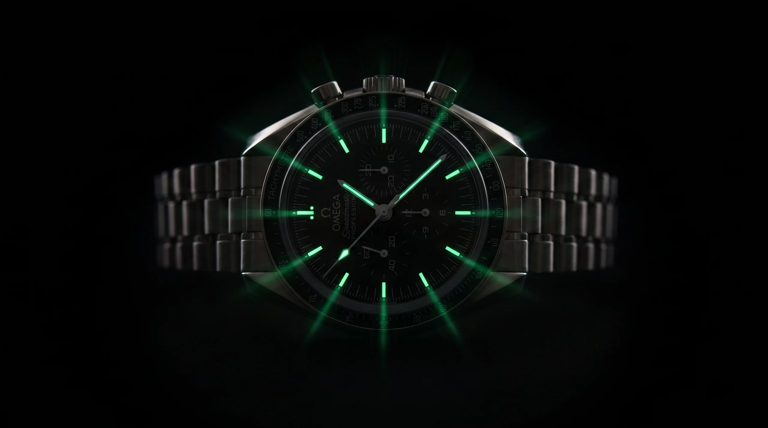 An Omega Speedmaster glowing green in the dark, its lumed hands and markers charged with light