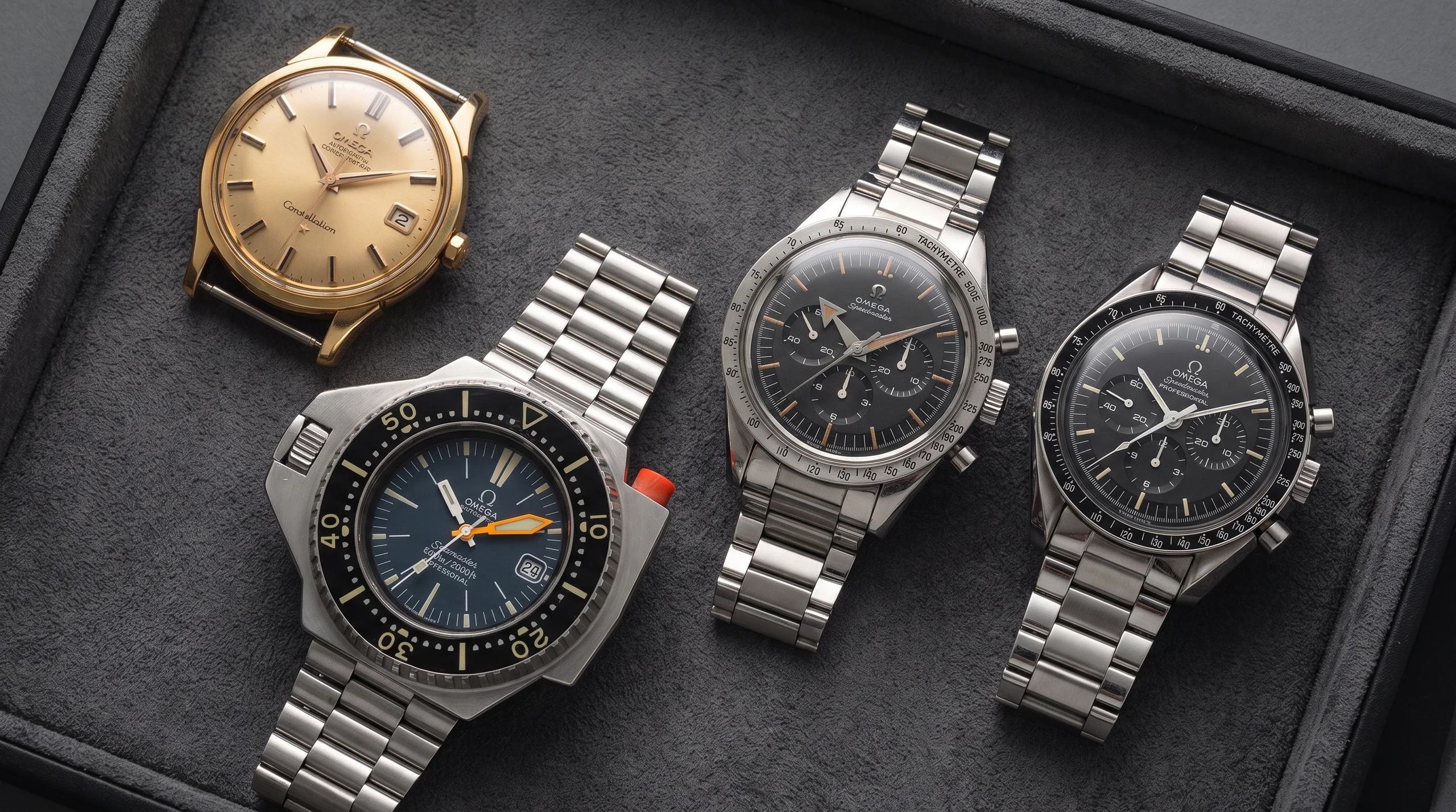 Four Omega watches on a display tray showing Pie Pan Constellation, PloProf, Broad Arrow Speedmaster, and Moonwatch chronograph
