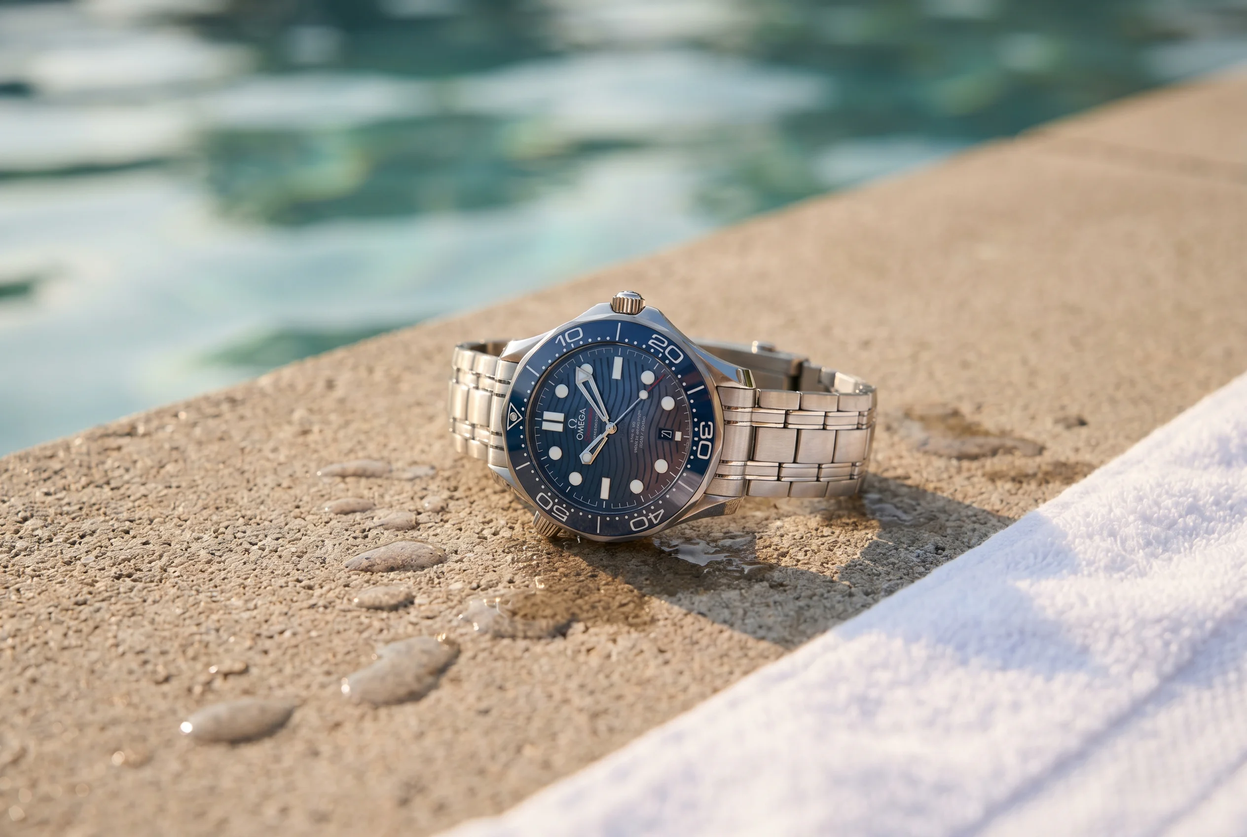 Modern Omega Seamaster Diver 300M reference 210.30.42.20.03.001 with blue ceramic bezel and wave dial resting on a concrete pool deck in late afternoon light