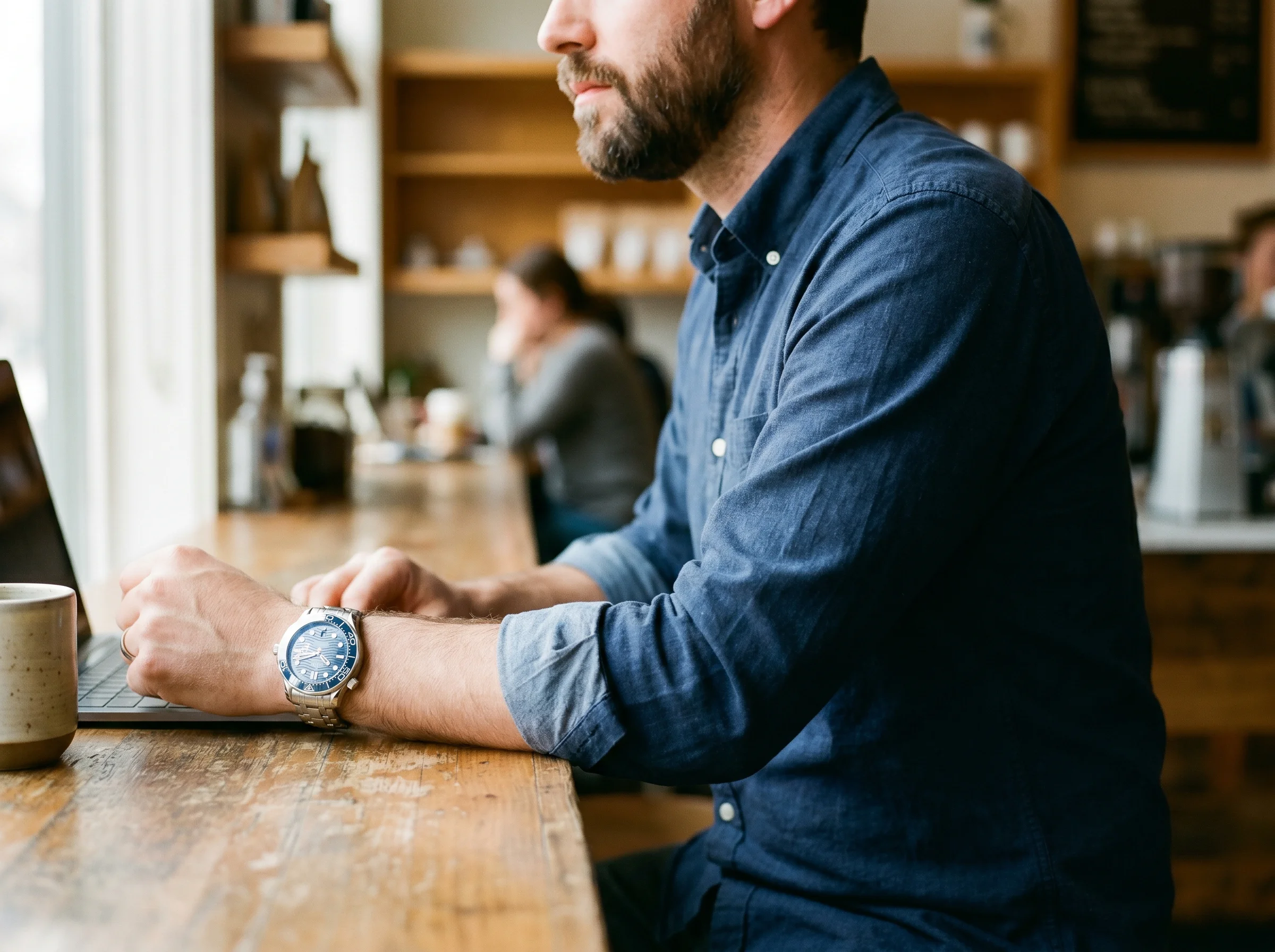 Modern Omega Seamaster Diver 300M reference 210.30.42 with blue ceramic bezel worn on a man's wrist resting on a coffee shop counter in natural daylight
