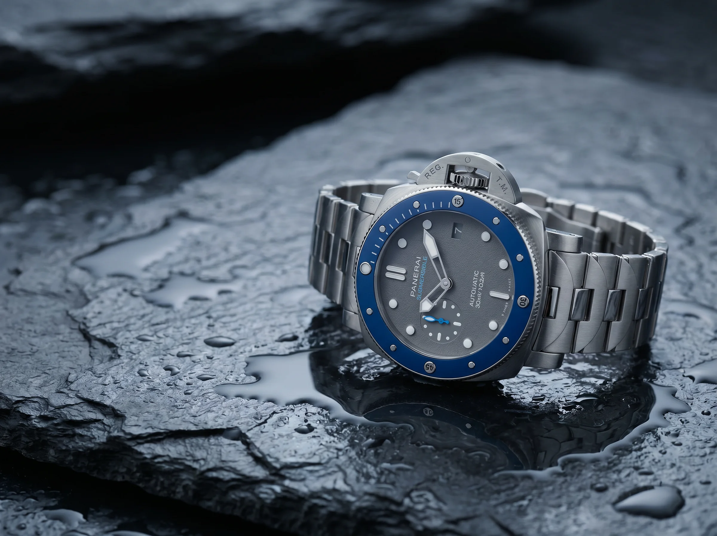 Submersible-style dive watch with a rotating bezel and crown-guard bridge resting on wet dark slate