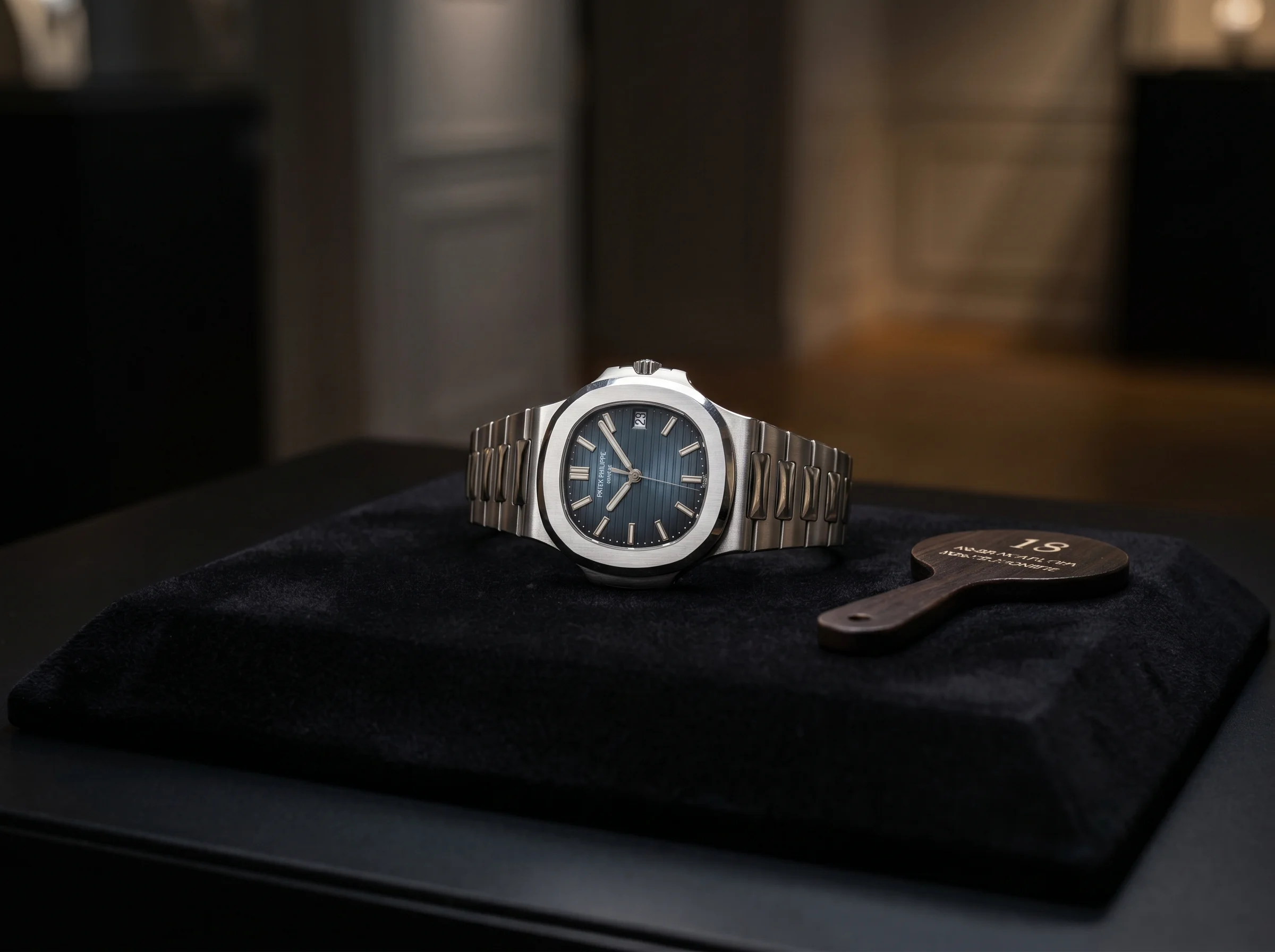Patek Philippe Nautilus 5711/1A on a black velvet auction pad beside a numbered paddle under gallery light