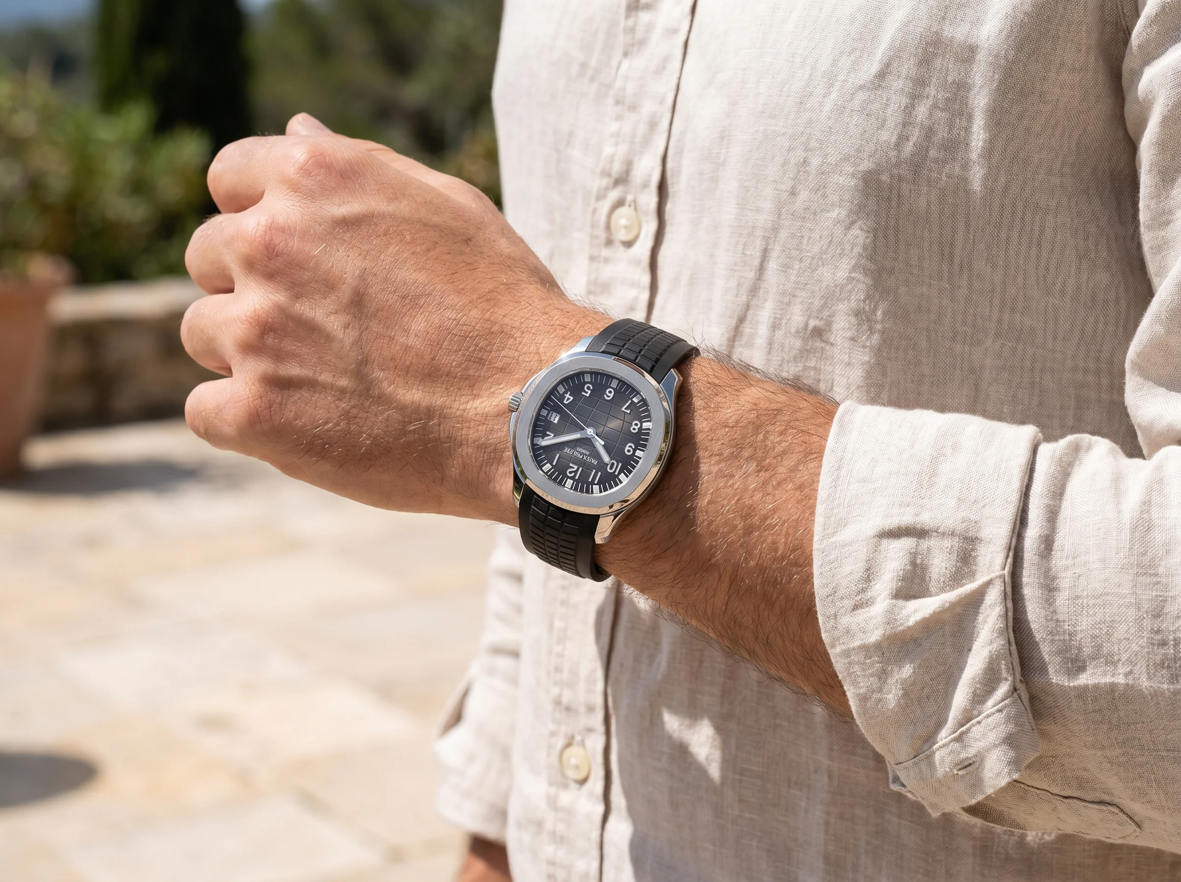 Luxury watch on a black rubber strap worn on a wrist over a casual sleeve