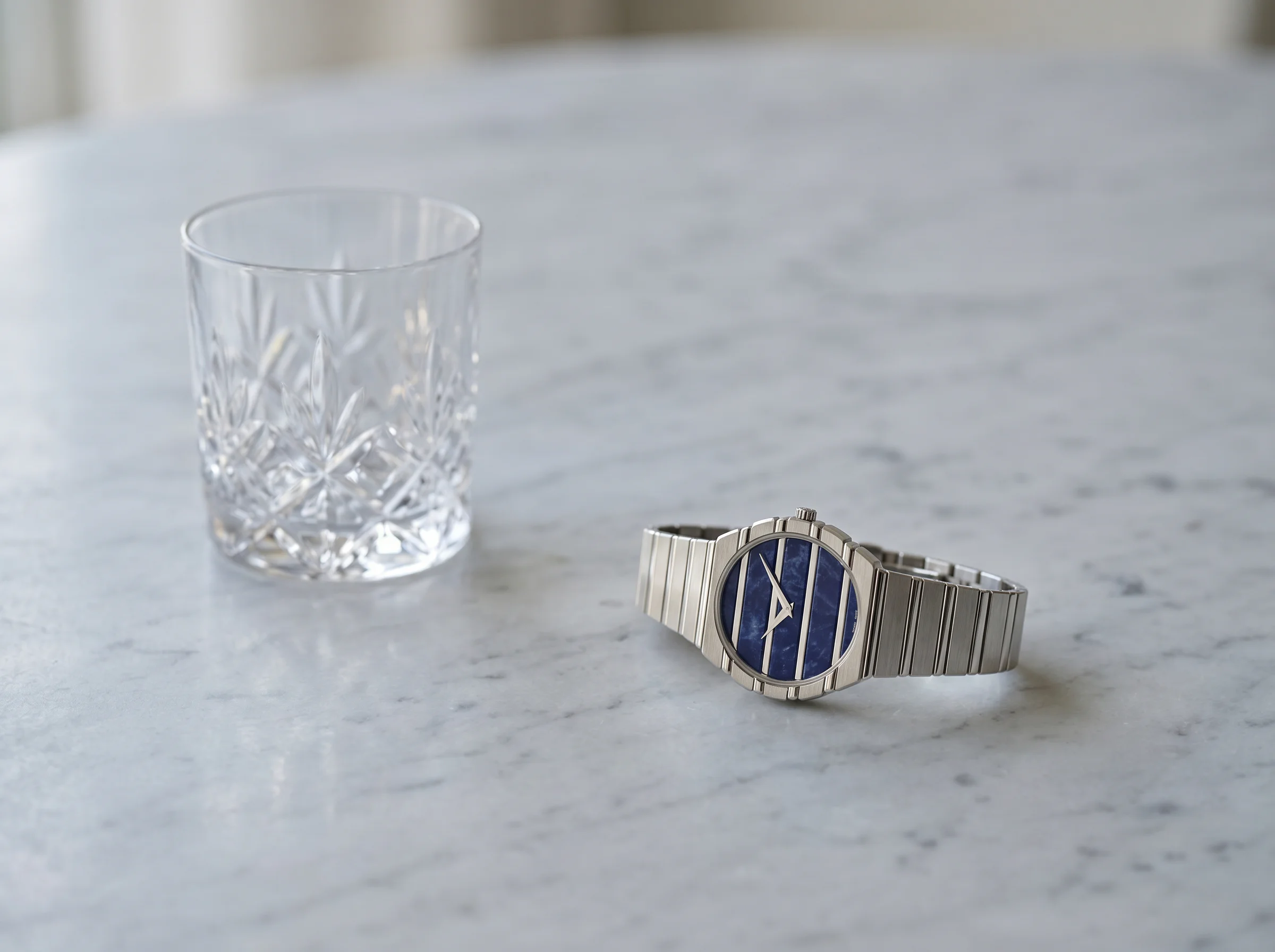 Piaget Polo 79 white gold with sodalite dial on grey marble beside a crystal tumbler