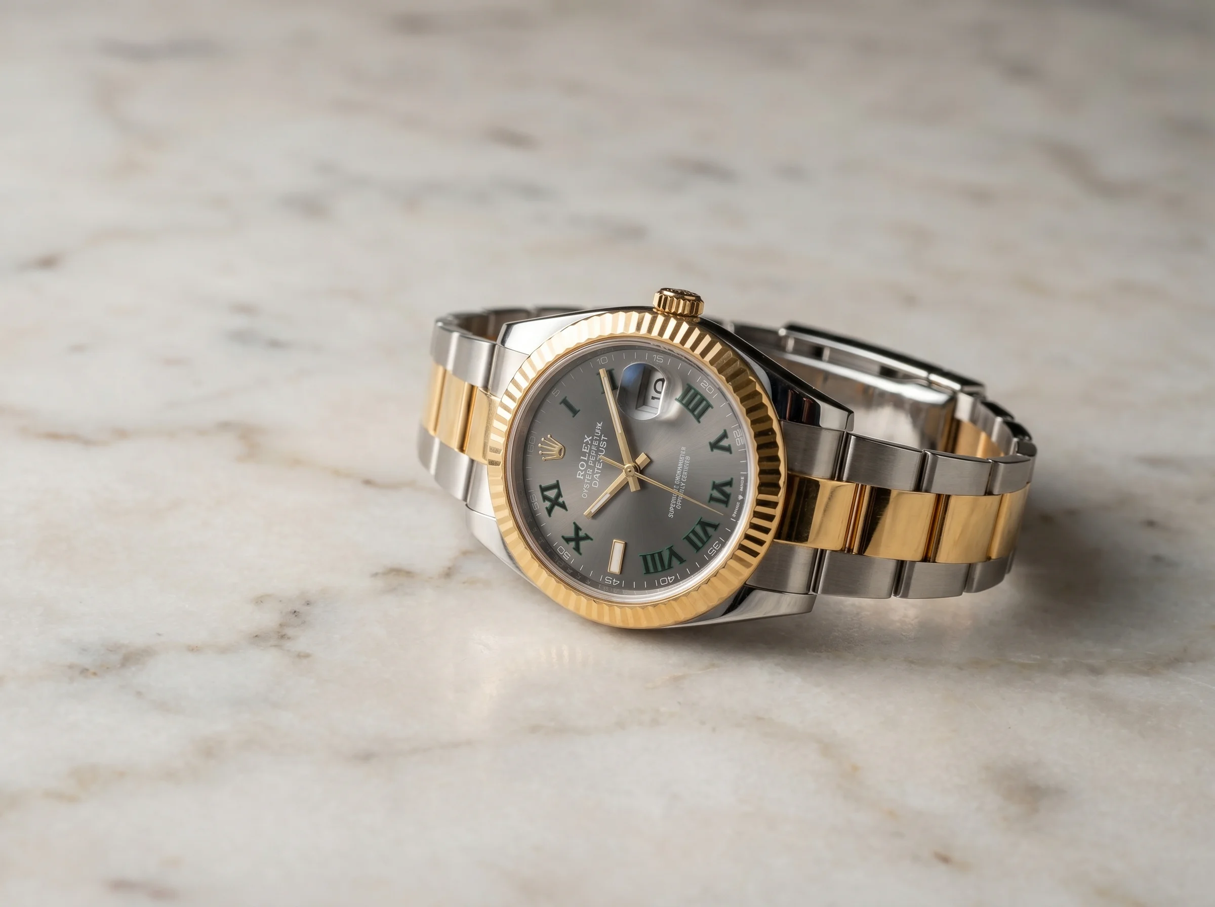 Two-tone steel and gold watch at a three-quarter angle on marble showing the gold bezel and gold centre links