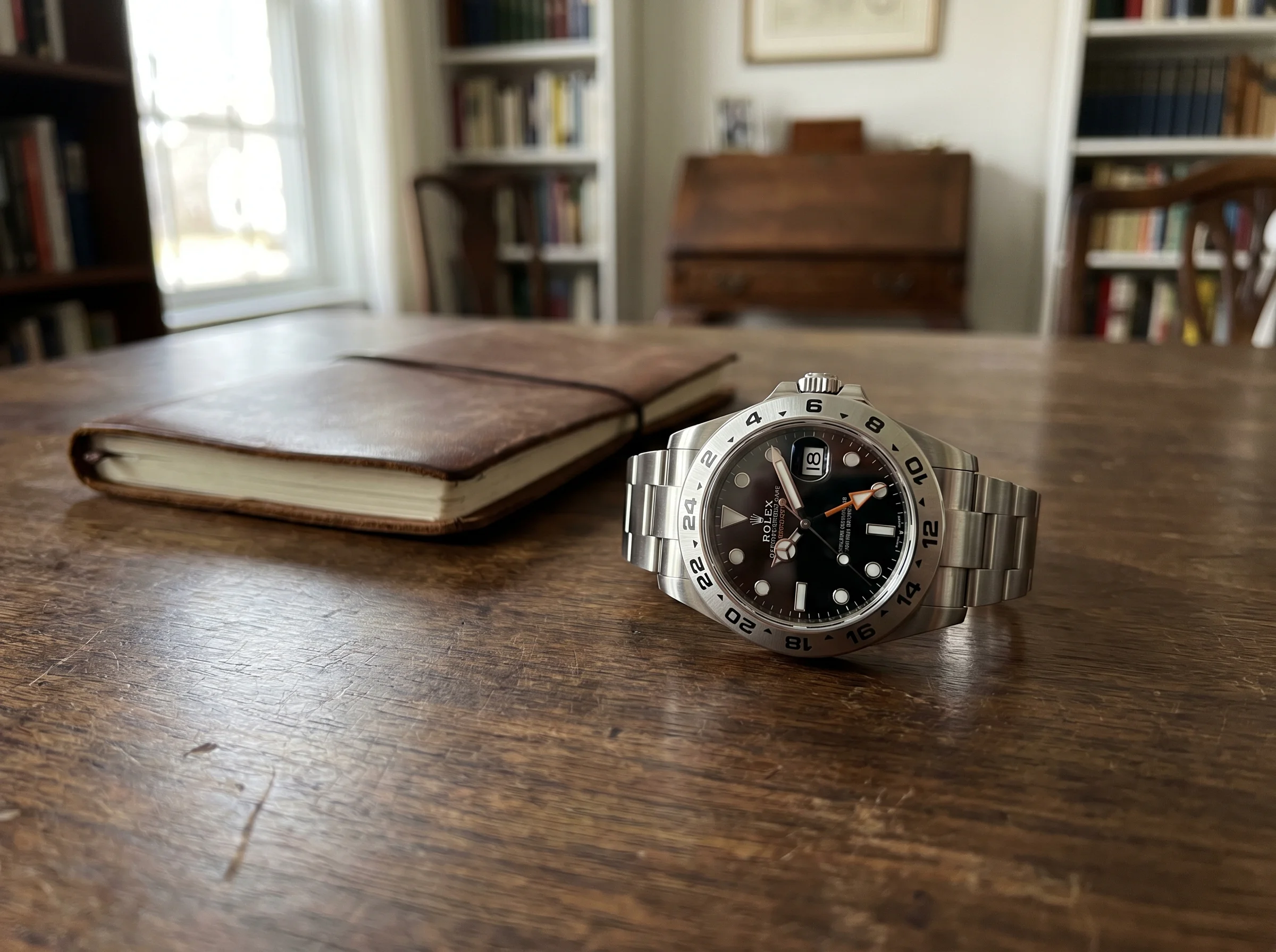 Rolex Explorer II 226570 with black dial and orange 24-hour hand on a walnut desk