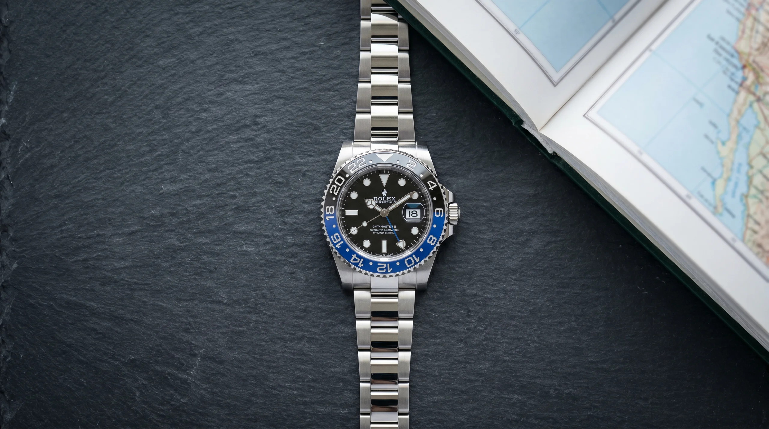 Top-down view of the Rolex GMT-Master II Batman reference 126710BLNR on a dark slate counter, the blue and black Cerachrom bezel current production GMT that absorbs displaced demand from the discontinued Pepsi 126710BLRO.