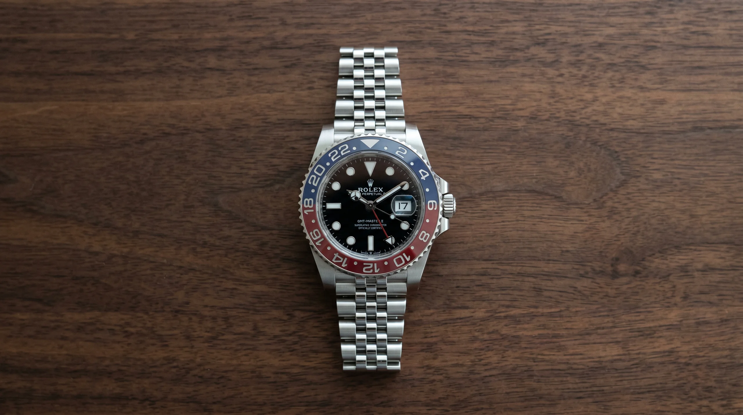 Top-down view of the Rolex GMT-Master II Pepsi reference 126710BLRO on a dark walnut surface, showing the blue and red Cerachrom bezel orientation with blue on the upper half from 12 to 6 o'clock clockwise and red on the lower half.