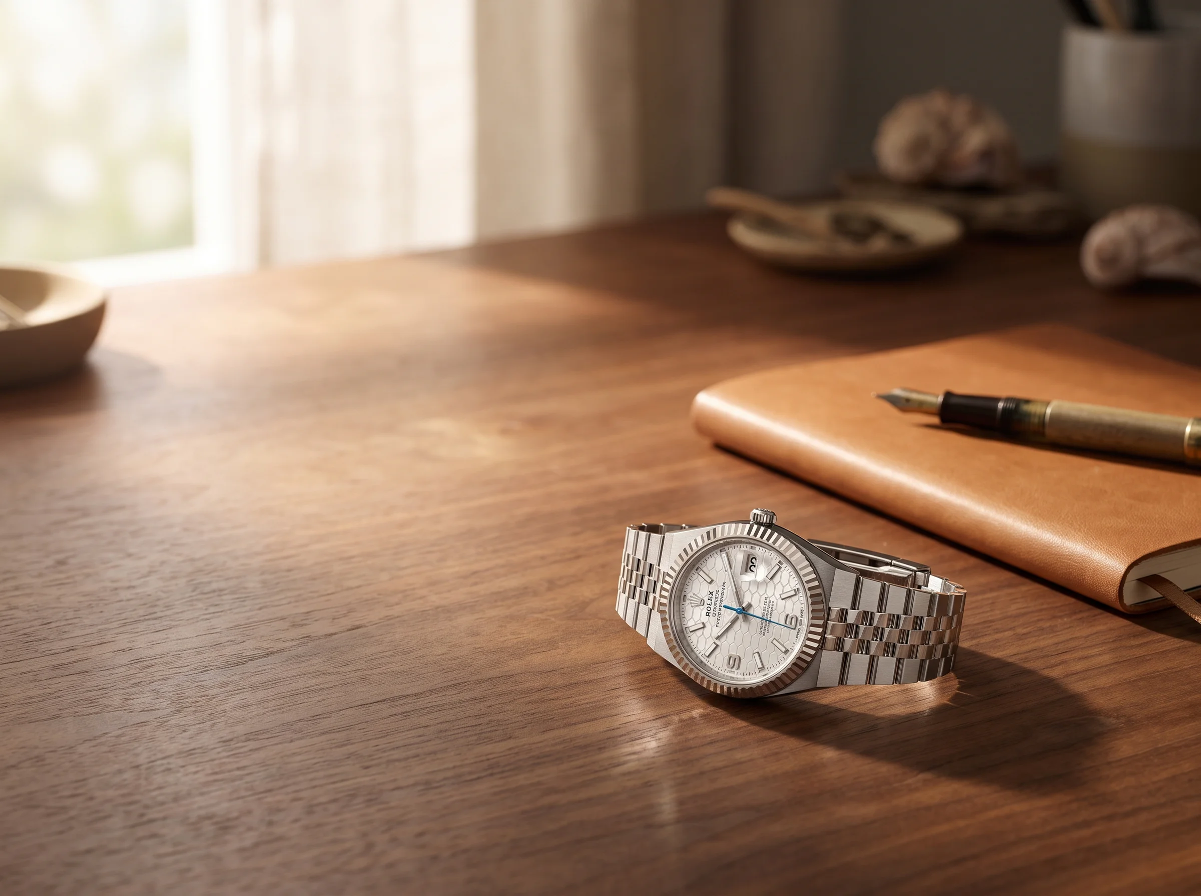 Rolex Land-Dweller wristwatch resting on a walnut desk beside a leather notebook and fountain pen in morning light