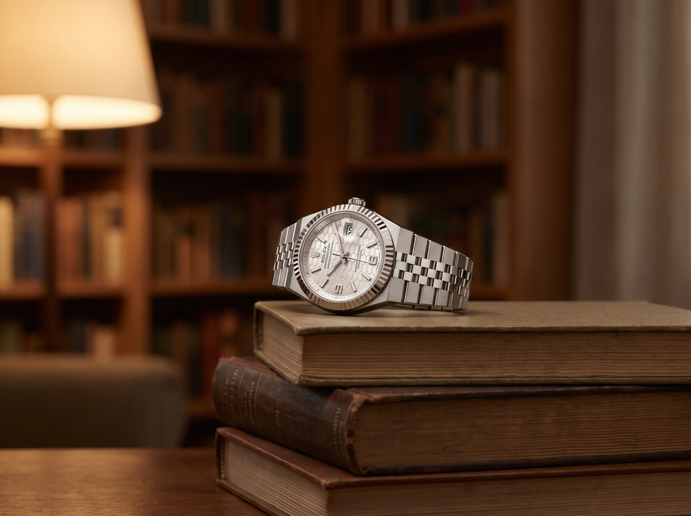 Rolex Land-Dweller resting at a three-quarter angle on a stack of hardcover books in a warm home library