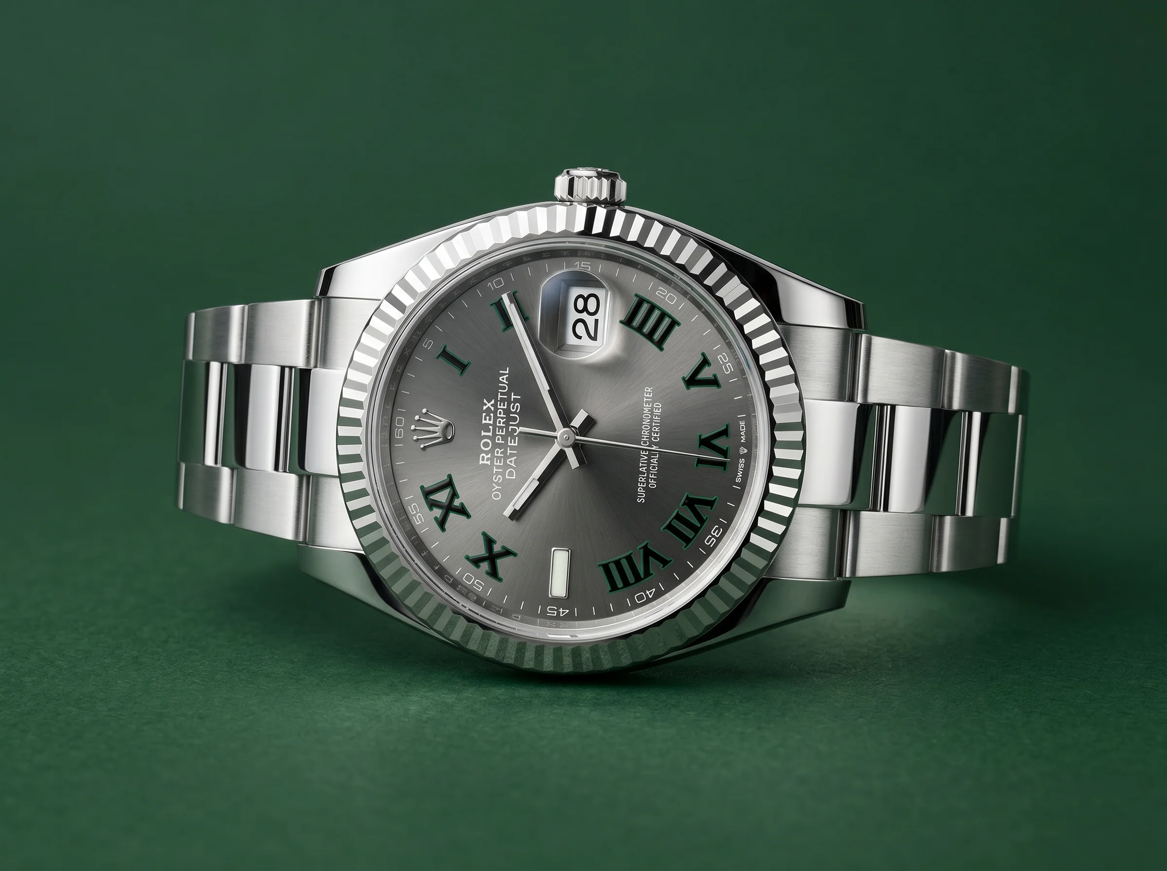 Studio shot of a steel Rolex Datejust Wimbledon with slate-grey dial and green-outlined Roman numerals on a deep green background