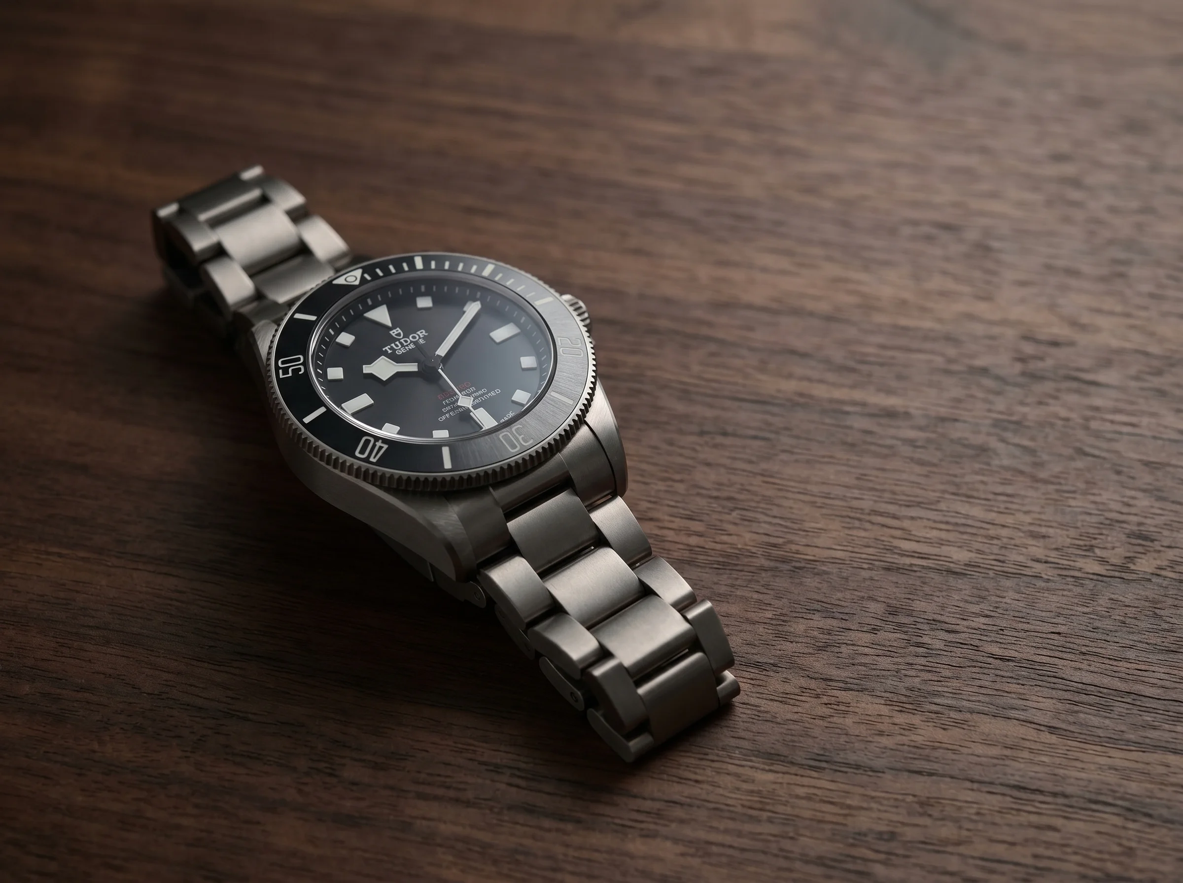 Matte titanium dive watch at a three-quarter angle on dark walnut