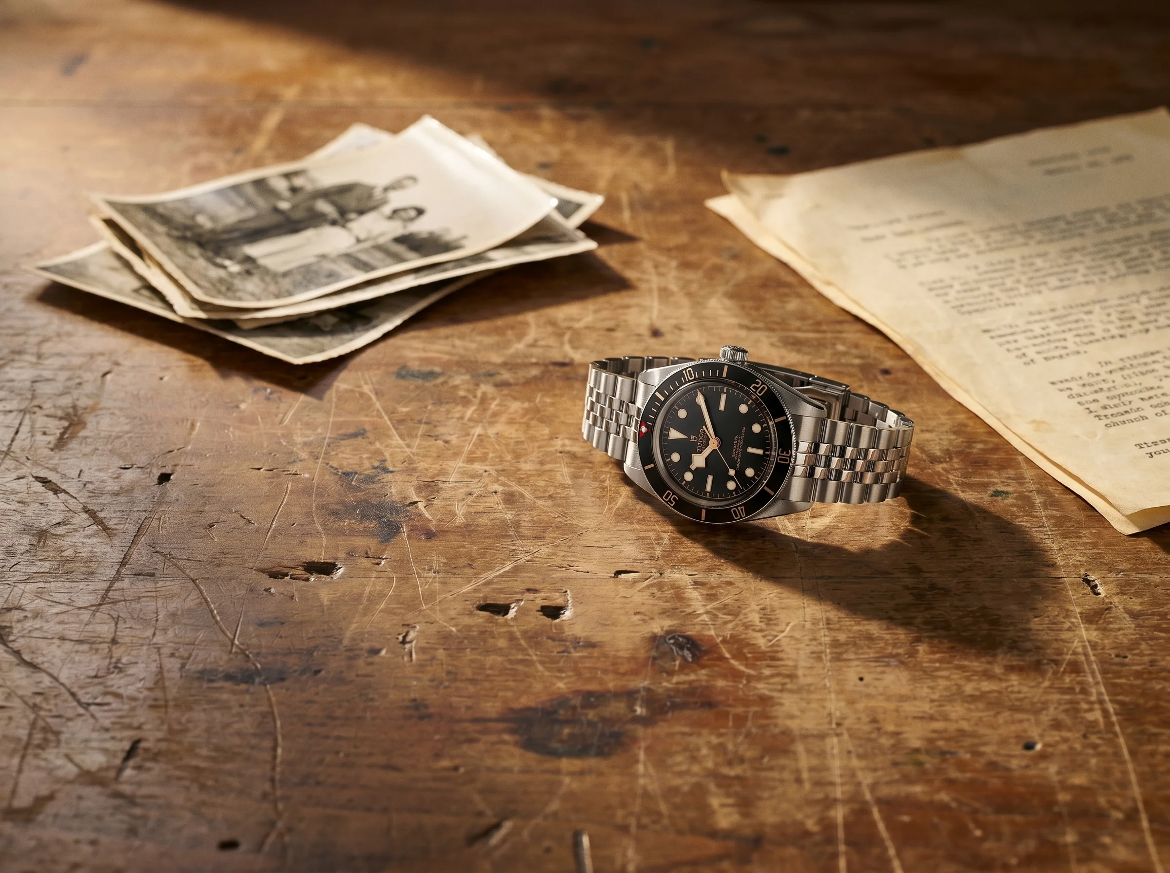 Tudor Black Bay 58 beside vintage photographs and an old document on a worn desk