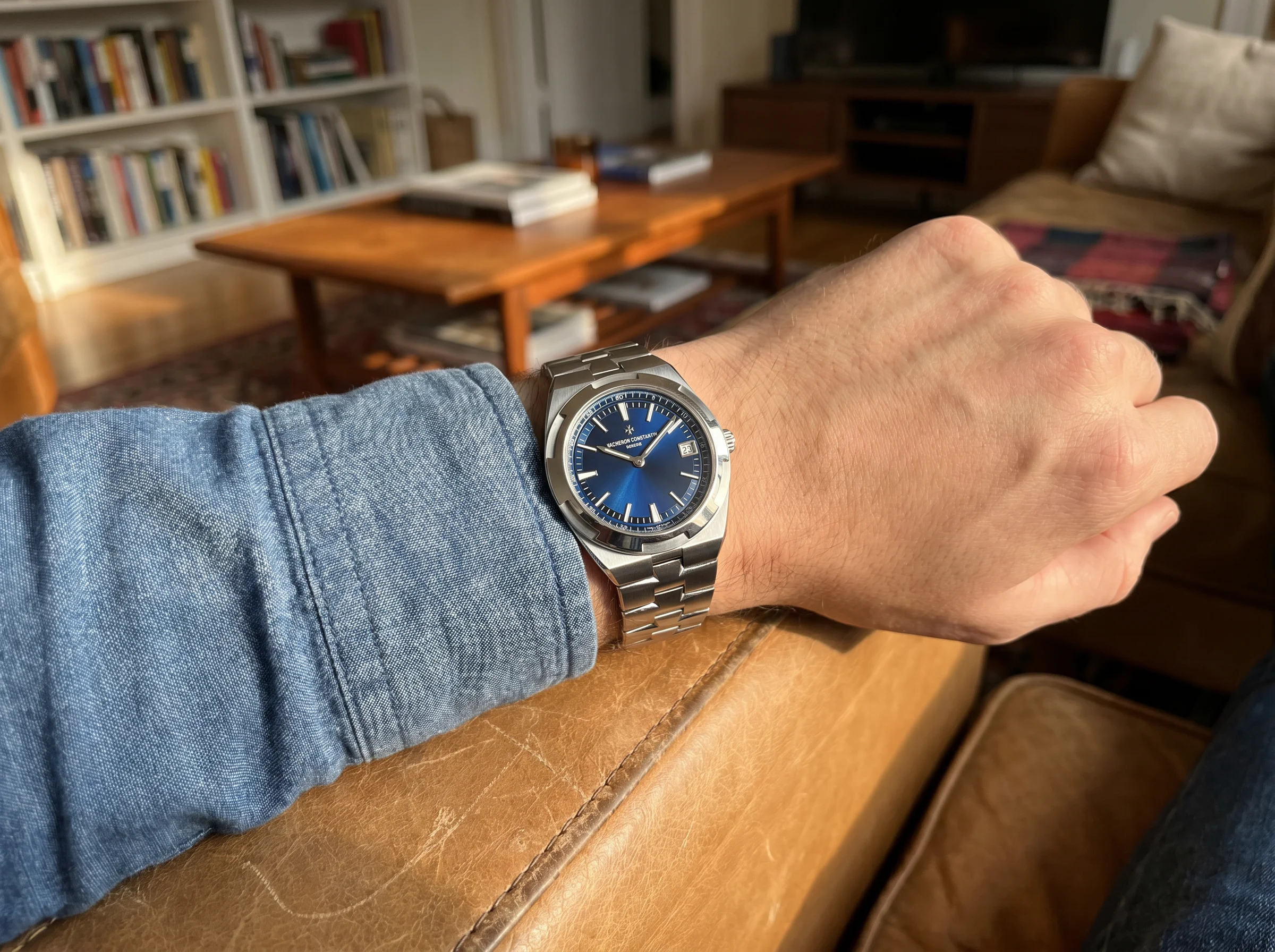 Vacheron Constantin Overseas with blue dial resting on a chambray shirt cuff on a tan leather chair