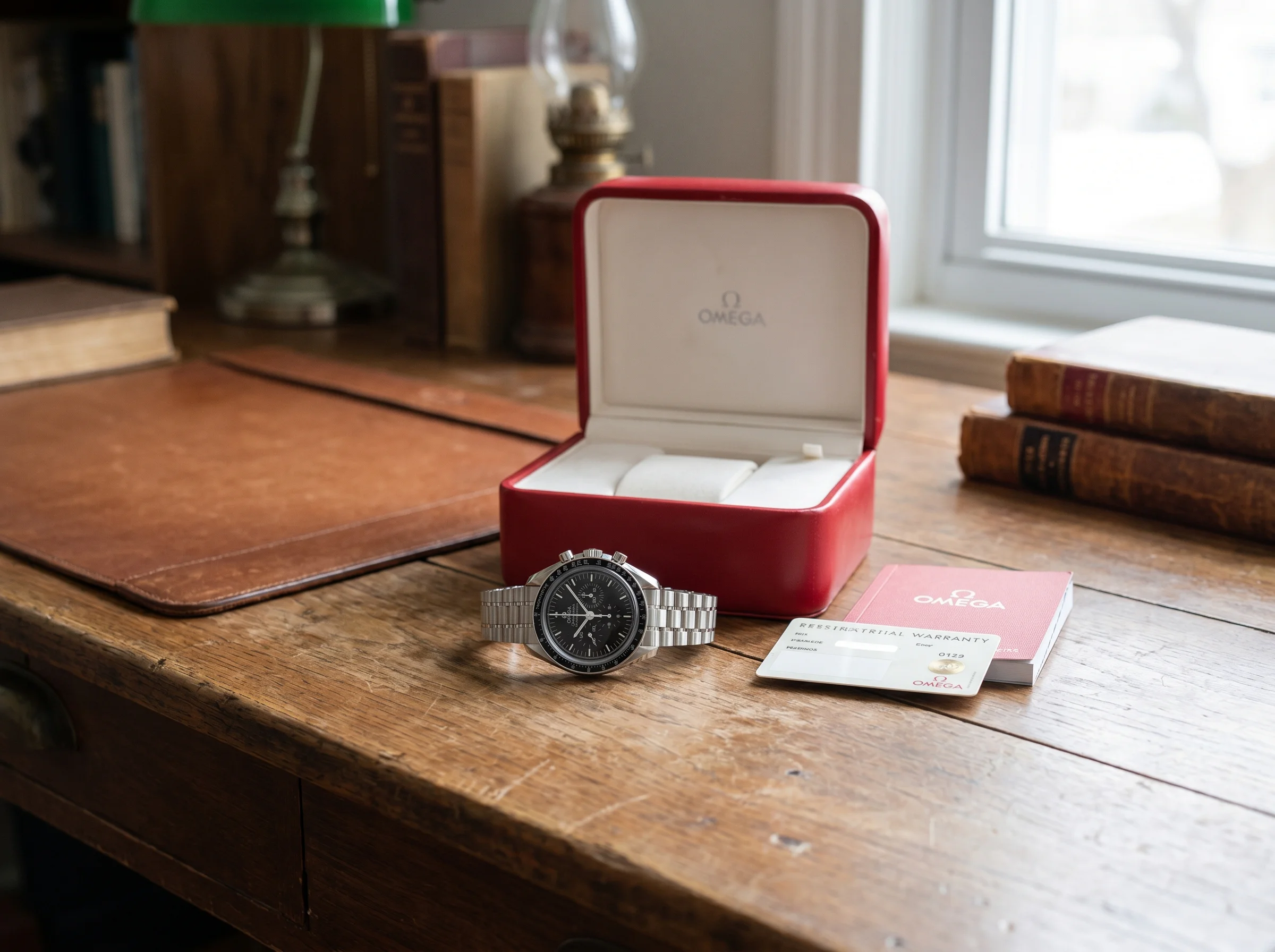 Omega Speedmaster Moonwatch Professional with its red Omega box, warranty card, and booklet on a desk