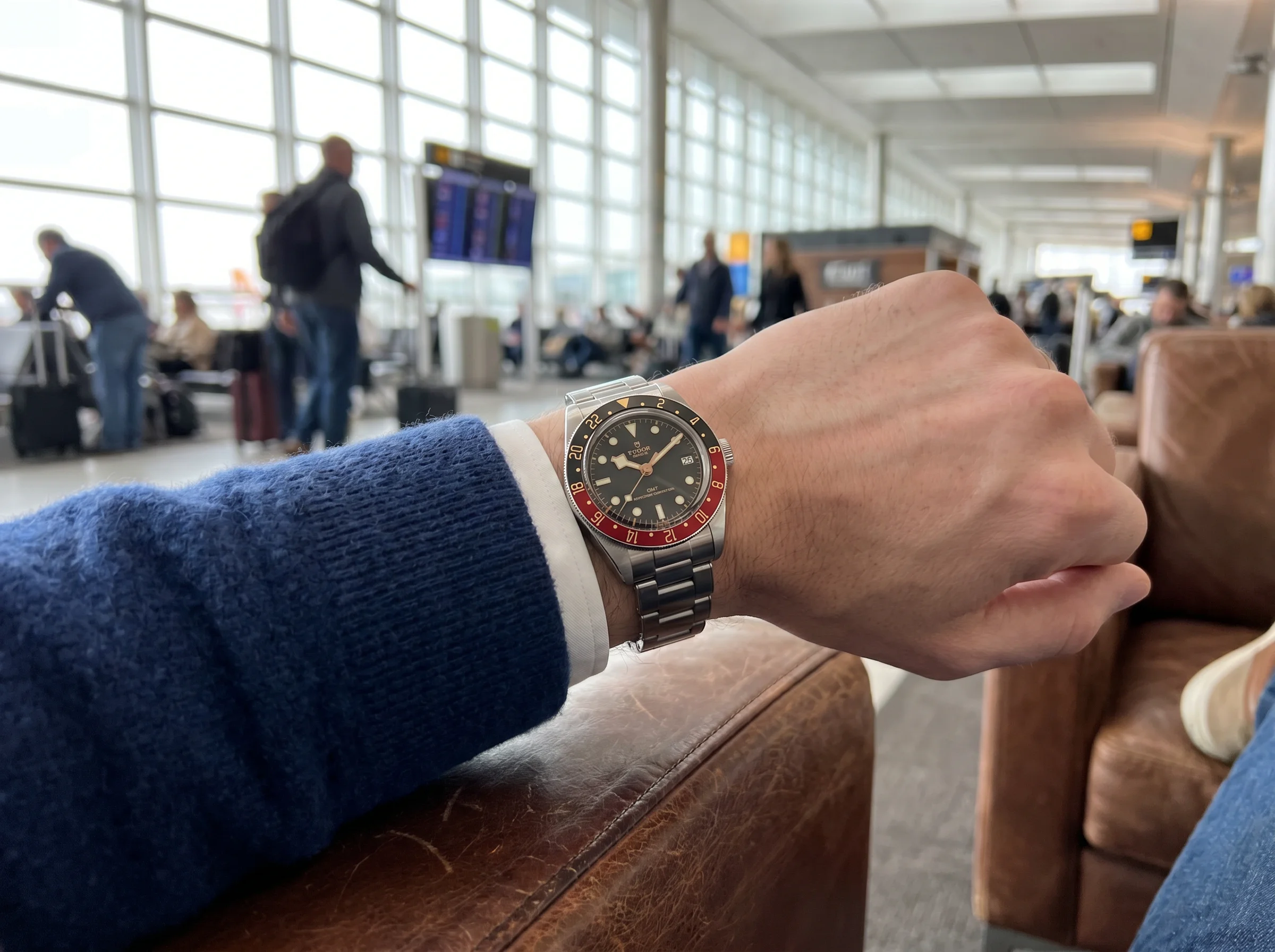 GMT watch on a wrist resting on a leather chair in an airport lounge